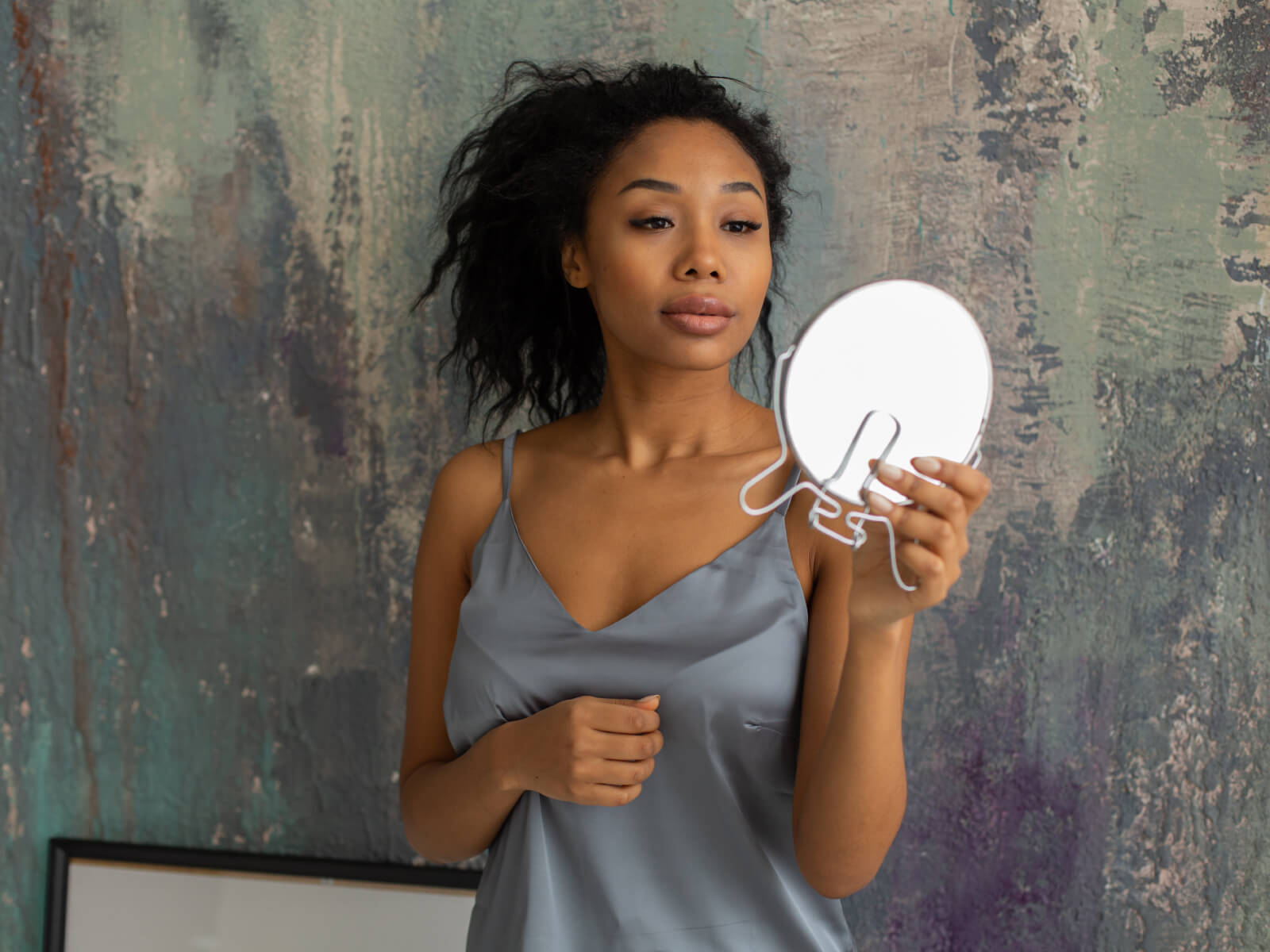 A woman holding onto a mirror while looking at her hair.