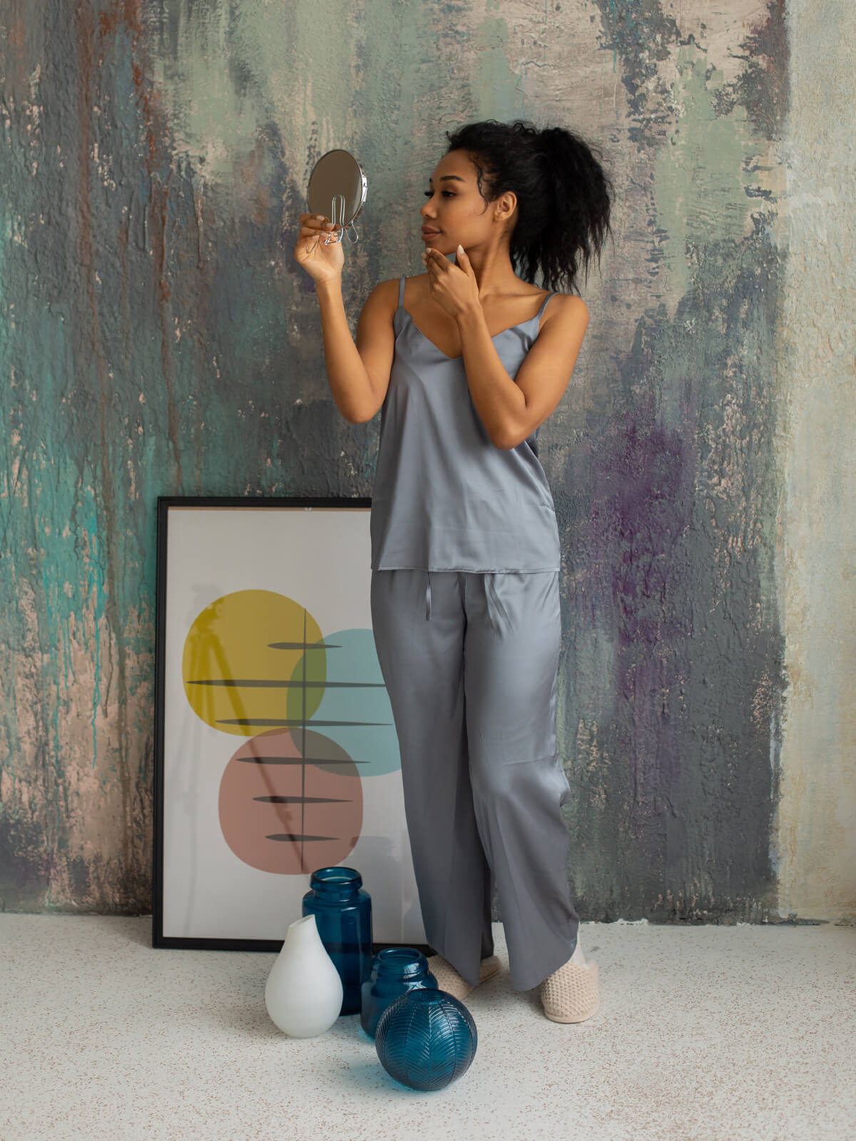 A woman in grey pajamas holding a mirror.