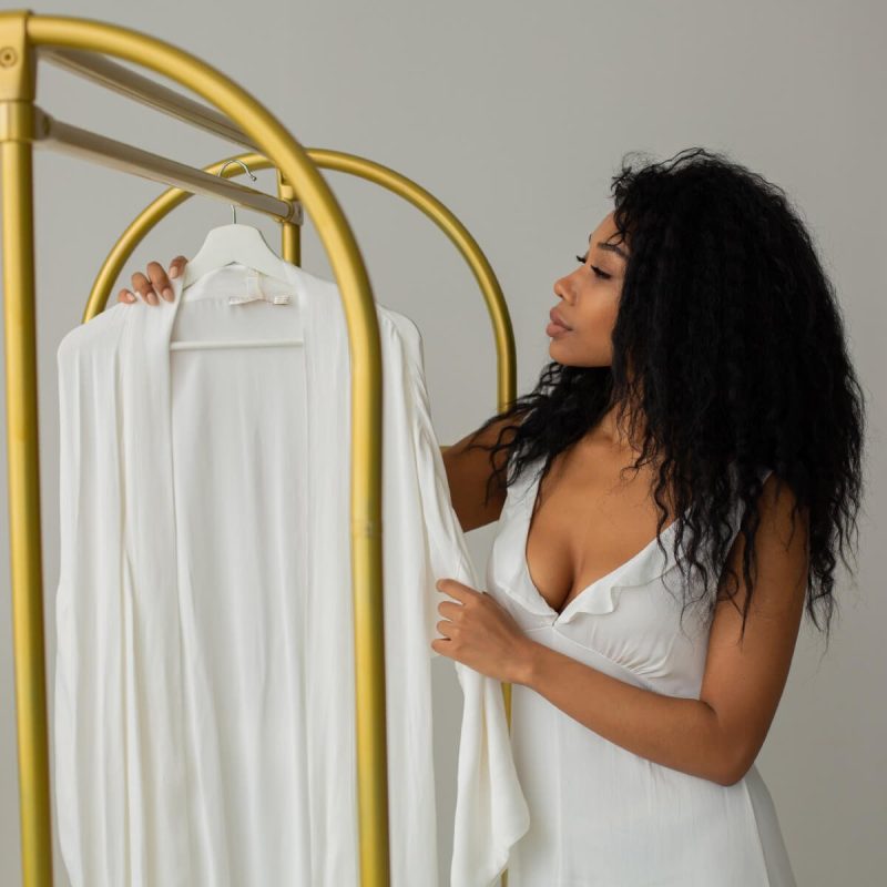 A woman holding up a white shirt on top of a rack.